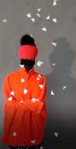 White three-dimensional foam flakes from Konzept-shop.de fall from the sky and land partly on a cut-out mannequin dressed as a winter sportswoman with a thick red fleece jacket and thick red woollen hat.