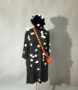 Fotografia de um manequim de costureira com um vestido preto e branco, um chapéu preto e um saco vermelho. O chapéu e o vestido estão cobertos por grandes flocos de neve tridimensionais, denominados TetraSnow. Foto: Leopoldi-Art.