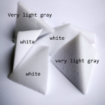 Detailed photo of König concept. Some tetrahedron-shaped foam flakes lie on a white surface so that you can clearly see the two shades of "white" and "light grey".